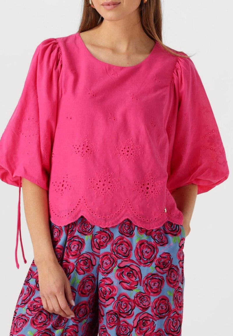 Roze blouse met geborduurde bloempatronen, korte pofmouwen, ronde halslijn en een gegolfde zoom, gecombineerd met blauwe bloemenprintbroek.