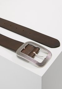Ceinture en cuir marron dotée d'une boucle en métal argenté de forme carrée, texturée avec un motif de points, et de plusieurs trous de fermeture le long de la sangle.