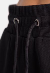 Melni sporta bikses ar ribotu jostasvietu un regulējamām auklām, kurām ir sudraba caurumi. Audums ir mīksts un gluds.