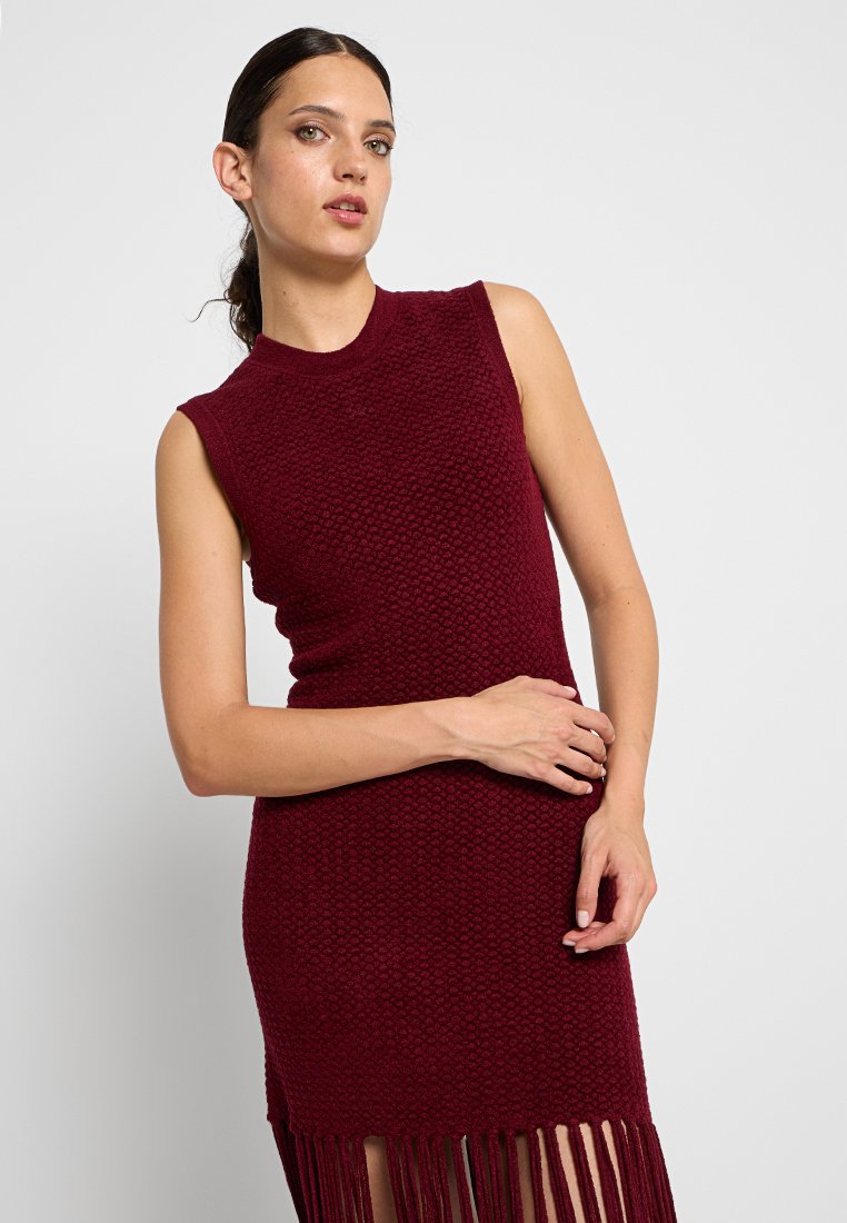 Vestido de punto burdeos con un escote alto, diseño sin mangas, tejido texturizado y detalle de flecos en el bajo.