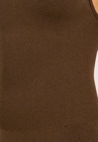 Brun rippad tanktop med en åtsittande design. Tyget är mjukt med en lätt glans och rena, minimalistiska detaljer.