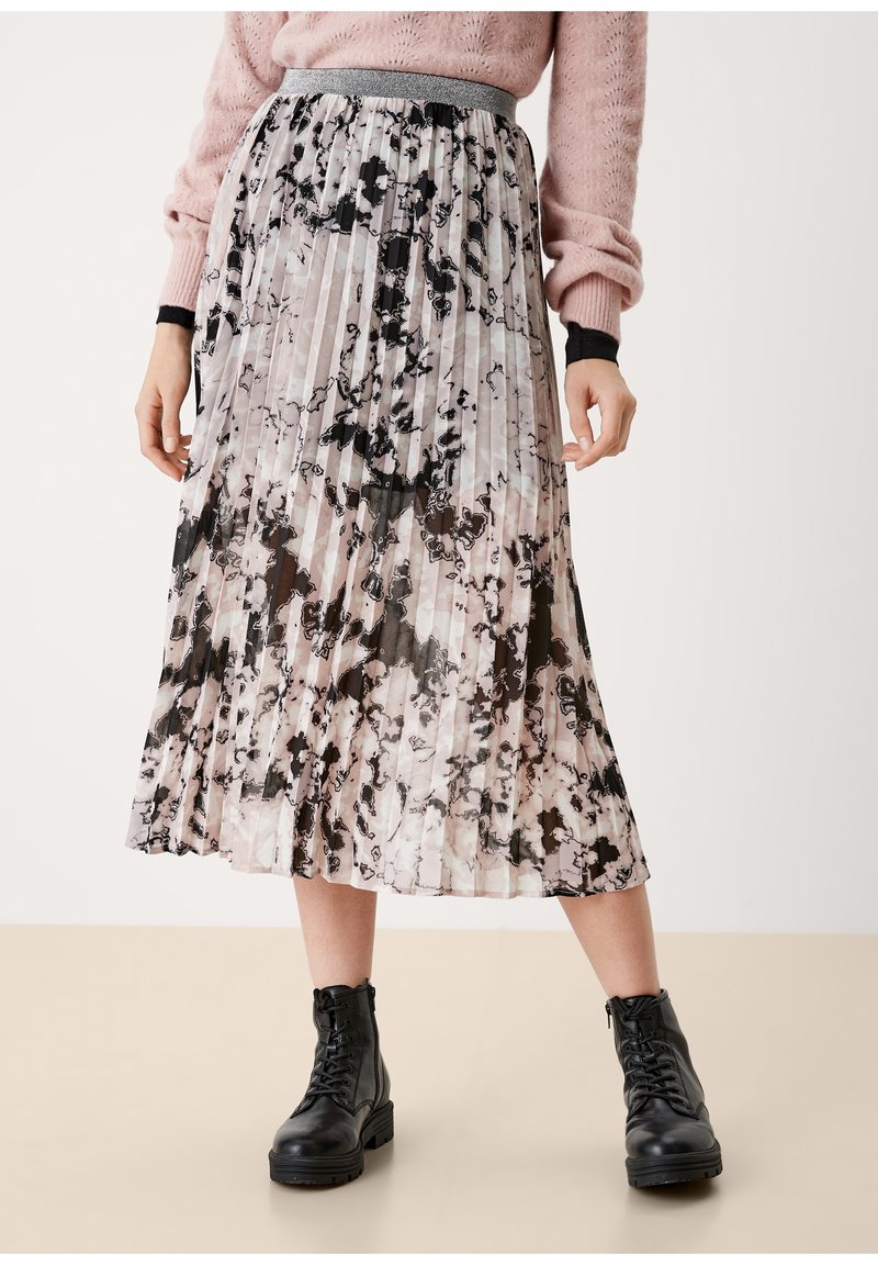 Femme portant une jupe midi plissée avec un motif abstrait noir et rose clair, associée à des bottines noires à lacets et un pull rose.