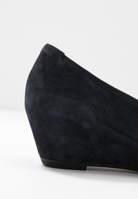 Scarpa con zeppa in suede blu scuro, caratterizzata da una punta arrotondata e una texture liscia, con una leggera elevazione nel tacco per un supporto aggiuntivo.