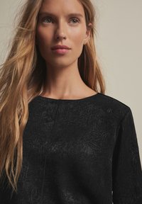 Black textured top with a rounded neckline, featuring crinkled fabric and long sleeves, creating a structured yet casual appearance.