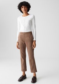 Top bianco a maniche lunghe con cucitura frontale, abbinato a pantaloni in suede marroni con taglio dritto e tasche laterali. Completato con mocassini neri.