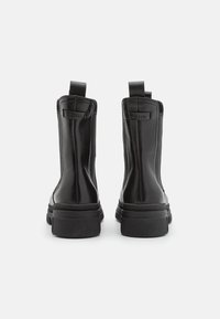 Černé kožené kotníkové boty s hladkým povrchem, elastickými bočními panely a poutky na zadní straně, s tlustou gumovou podrážkou.