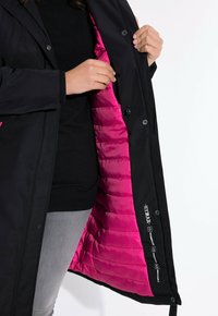 Musta vedenpitävä takki, jossa on kirkkaan vaaleanpunainen vuori. Ominaisuuksiin kuuluu napitus, sisätasku ja logot sisähelmassa.