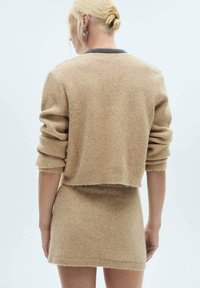 Beige kort tröja över en matchande minikjol, tillverkad av mjukt stickat material, med rullade ärmar och ribbad nederkant. Enkel design.