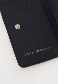 Marineblå lær Geldbörse med guldfarvede detaljer, der har kortlommer og præget logo "TOMMY HILFIGER" på den ene side.