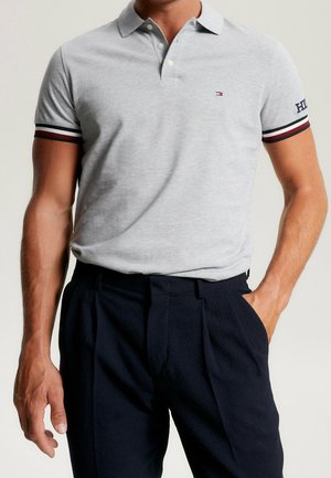 Grå polo shirt med krave, der har stribede manchetter i navy og rød, parret med mørke, strukturerede bukser.