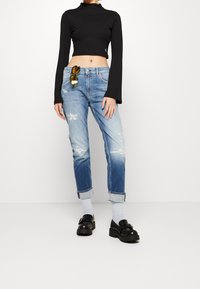 Mustapintainen ribattu pitkähihaine crop-top, vaaleansiniset kuluneet farkut käännetyllä helmalla, mustat paksupohjaiset loaferit, keltaiset aurinkolasit vyötärönauhalla.