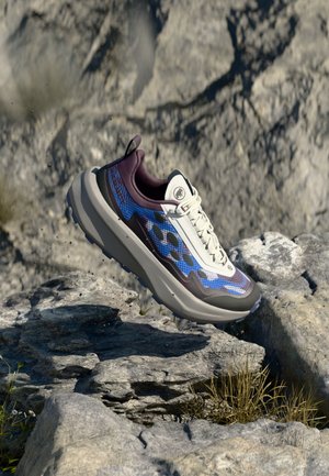 Athletic shoe with a mixed material upper in blue and white, padded collar, textured sole, and elevation in design. Accented by purple details.