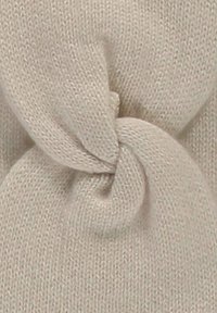 Beige knitted fabric featuring a twisted knot detail, displaying soft texture and woven pattern throughout.
