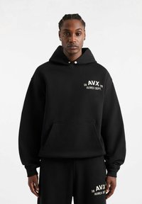 Felpa nera con tasca frontale e cappuccio con stringa. Presenta la scritta bianca "AVX 1975 AVIREX DEPT." sul petto. Tessuto morbido e texture.