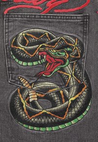Black denim pocket featuring detailed snake embroidery in green, yellow, and red, with a textured, swirling pattern and contrasting colors.