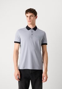 Grå polo-skjorte med svart krage og mansjetter, med tre knapper og brodert logo på brystet. Glatt stofftekstur.