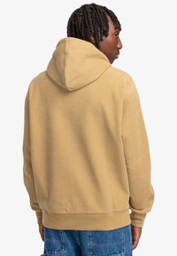 Khaki corduroy hoodie with a hood and ribbed texture; features a relaxed fit and long sleeves, styled with a waistband at the hem.