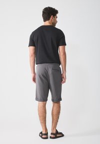 Svart T-skjorte med korte ermer og grå knelengde shorts med rullekanter. Shortsene har en baklomme og en myk tekstur. Sandaler blir brukt.