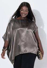 Metallisch graues Oversized-Oberteil mit glatter Textur, kurzen Ärmeln und weitem Ausschnitt, kombiniert mit einer mit Pailletten besetzten Clutch und Armreifen.