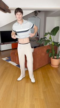 Chemise polo à manches courtes, à rayures grises ; pantalon beige avec une boucle de ceinture à l'avant et une boucle latérale ; baskets blanches ; cadre intérieur avec une plante verte.