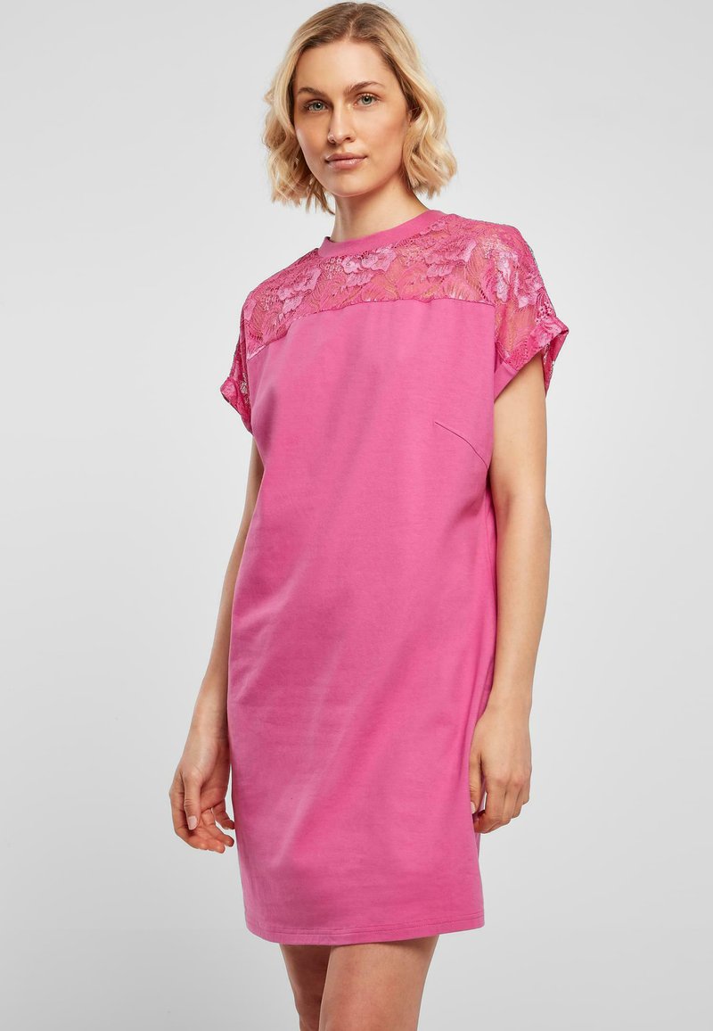 Roze jurk met een kant yoke, korte mouwen en een relaxte pasvorm. Inclusief een zak aan de voorkant, gemaakt van zachte, ademende stof.