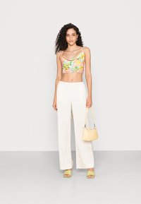 Top cropped com estampado floral em cores pastel, combinado com calças largas brancas, bolsa amarela e sapatos de salto abertos verdes. Textura suave.