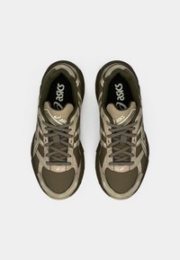 Brune og beige treningssko med nett og syntetiske materialer, med et strukturert design, snørebånd og logo detaljer.