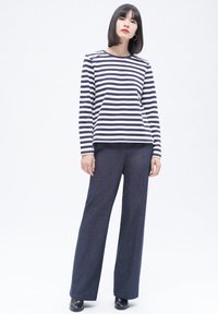 Marineblauwe en witte gestreepte langemouwen top met schouderaccenten, gecombineerd met losse donkere broeken en zwarte haklaarzen.