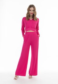 Fuchsia crop top met lange mouwen en een uitsnijding bij de taille, gecombineerd met wijde broekspijpen. Glad stof, elastische tailleband en zijzakken.
