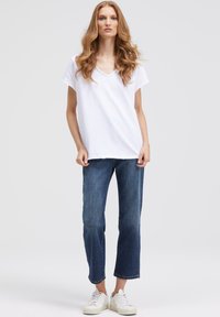 White short-sleeve v-neck t-shirt paired with blue straight-leg jeans and white sneakers, featuring a relaxed fit and soft fabric texture.