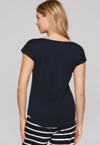 Navy blue short-sleeve top with a wide neckline, soft fabric, and a rounded hem, paired with striped black and white pants.