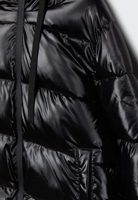 Svart puffjacka med glansigt ytskikt, breda horisontella sömmar, dragkedja framtill och svarta dragskor vid halsen.