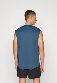 Sleeveless, dark blue athletic shirt with a round neckline and extended armholes. Fabric appears lightweight with a smooth texture.