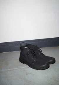 Černé vysoké tenisky z plátna s kulatým logem, šněrovací design, gumová špička a texturovaná podešev. Minimalistický styl bez vzorů.