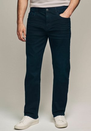 Donkerblauwe denim jeans met een rechte snit, vijf-pocket ontwerp en een knoopsluiting. G gedragen met witte sneakers voor contrast.