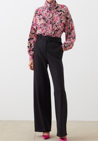 Floral print blouse in pink and black, featuring a high collar and loose fit, paired with black high-waisted trousers and pink heels.