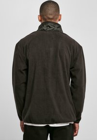Brun fleecejakke med ståkrage, med en glatt tekstur, lange ermer og en avslappet passform. Ingen synlige logoer eller mønstre.
