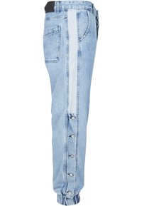 Jeans din denim bleu deschis, cu un panou lateral contrastant, accente cu nasturi pe picior și un design cu tiv tapered la gleznă.