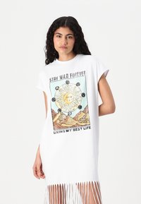 Balta didelio dydžio t-shirt su frakcionu apvadu. Pabrėžia spalvingą saulės ir kalno grafiką su tekstu "IŠLIK KIKS BUVIMAI" ir "GYVENNU GERIAUSIĄ GYVENIMĄ".