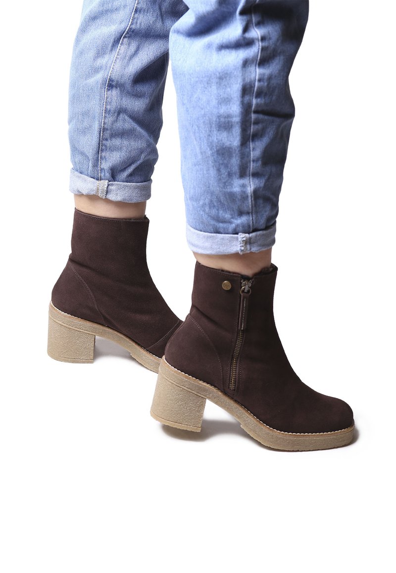Stivaletti in suede marrone con punta arrotondata e zip laterale. Presentano un tacco spesso e texturizzato e una suola piatta beige.