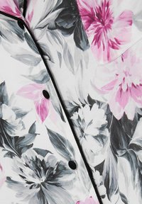 Květinová blůza s růžovými a šedými květinami na bílém pozadí, s černými knoflíky a lemem. Materiál má hladkou strukturu.