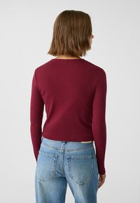 Bordeaux lange mouwtop met een geribbelde textuur, ronde halslijn en een getailleerd ontwerp, gecombineerd met lichtblauwe hoge taille jeans.