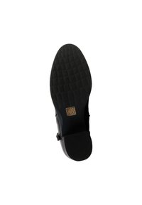 Semelle de chaussure noire avec motif de grip texturé et petite étiquette carrée, vue du dessous sur fond blanc.