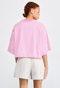 Camicetta corta con righe verticali rosa e bianche, maniche corte e vestibilità rilassata. Abbinata a pantaloni corti a righe grigie chiare e bianche.