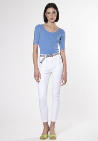 Top de punto acanalado azul claro con mangas cortas, jeans skinny blancos y sandalias de tacón verde. Cuenta con un cinturón decorativo.