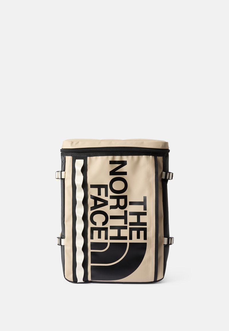 Béžový batoh s černými akcenty, s výrazným logem a grafickým designem, zipovým uzávěrem a nastavitelnými popruhy pro funkčnost.