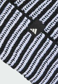 Primer plano de tela de punto a rayas negras y blancas con una pequeña etiqueta negra que muestra el logo blanco de Adidas.
