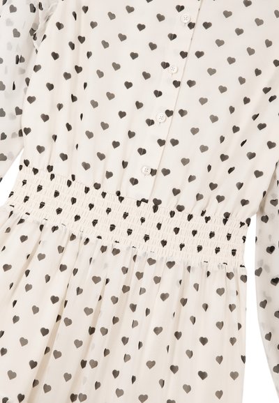 Cremfarbenes Kleid mit schwarzem Herzmuster, Knopfleiste vorne, geraffter Taille und gesammeltem Rock. Glatter Stoff mit transparenten Ärmeln.