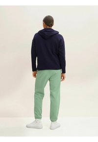 Granatowy dres z kapturem i kieszenią kangurką, w komplecie z jasnorozowym dresami z elastycznymi mankietami. Całość dopełniają białe trampki.