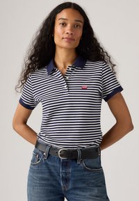 Randig polo t-shirt i marinblått och vitt, kortärmad med krage. Röd Levi's-logga på bröstet. Bärs med jeans i denim och ett svart bälte.